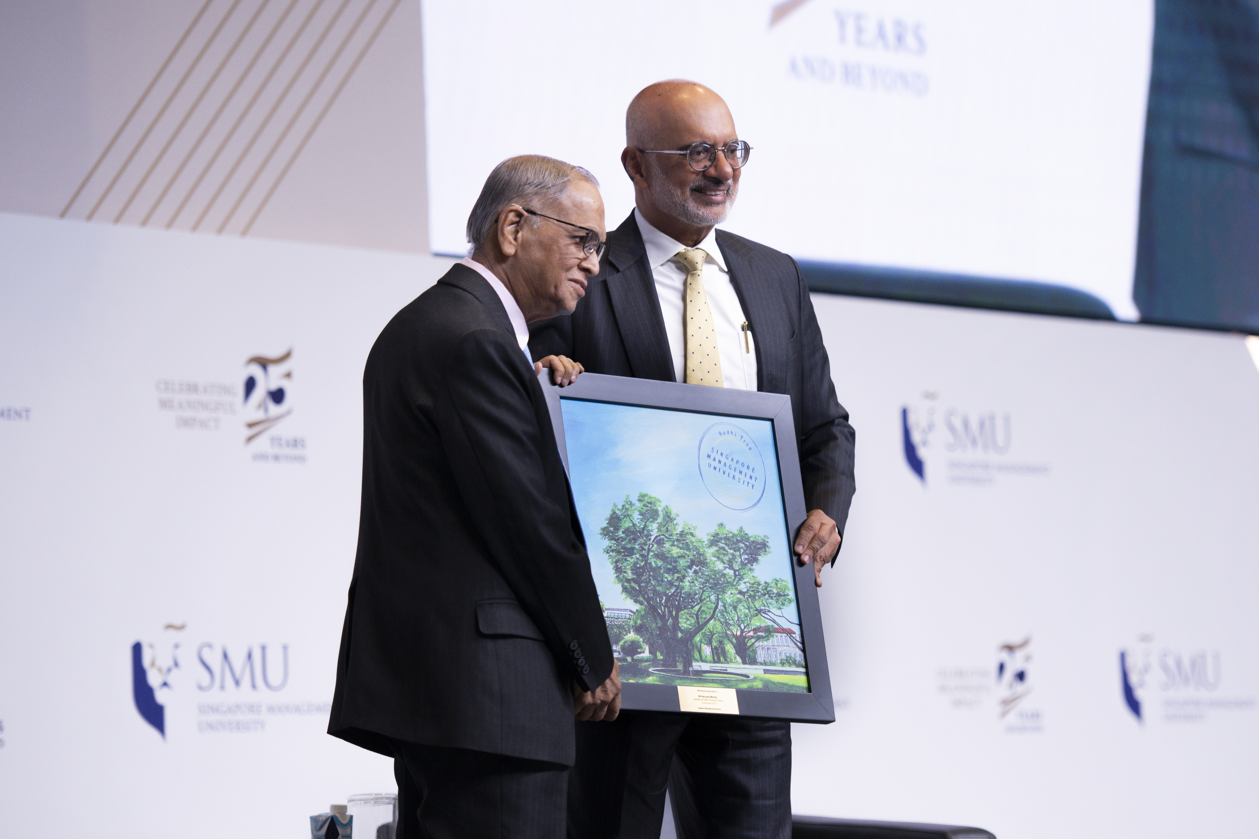 Mr Piyush Gupta (right) presenting a painting to Mr Murthy (left) a painting by SMU alumna Kelly Ser. The artwork depicts the iconic Bodhi Tree on SMU Campus which sympolises wisdom, compassion and hope.