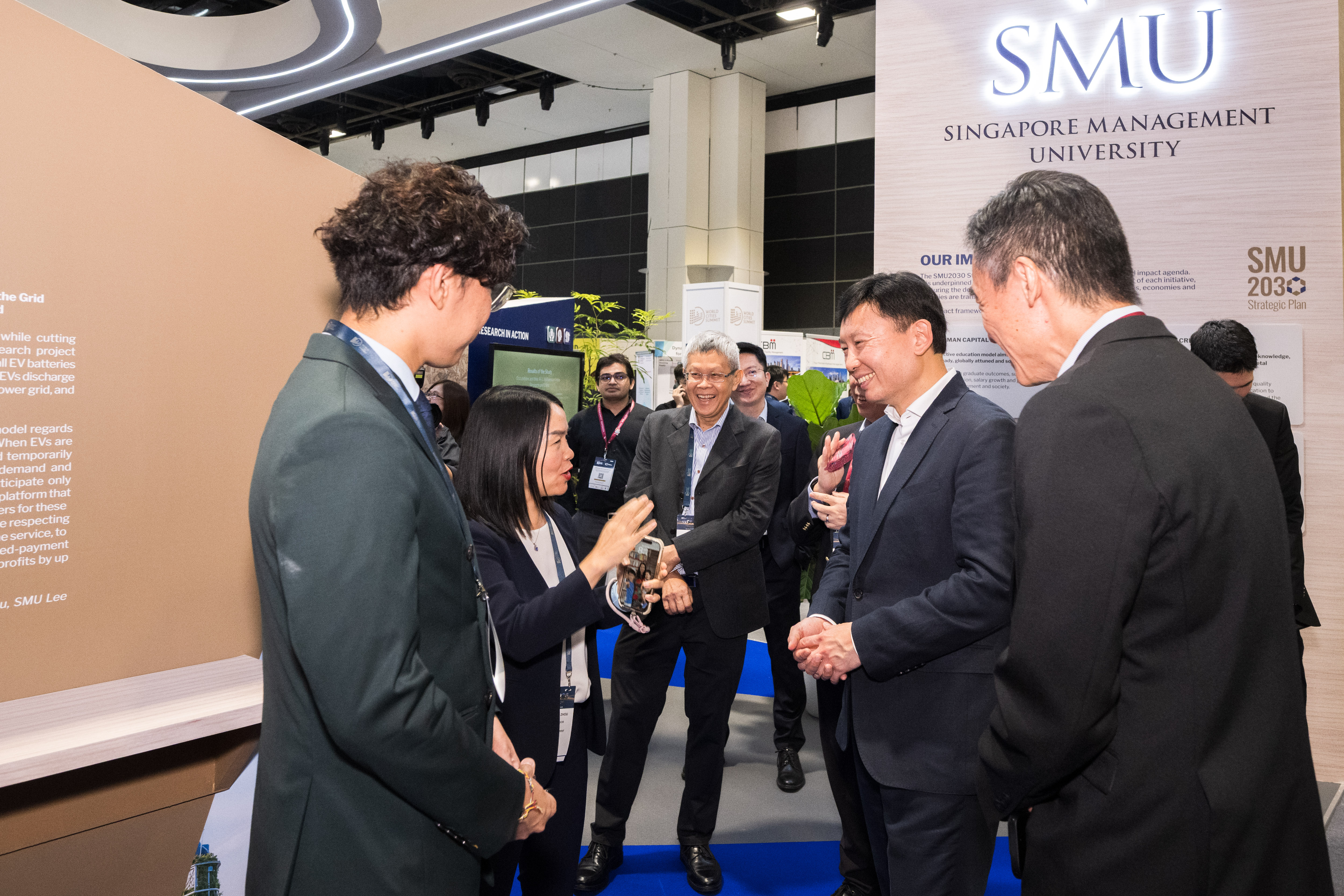 Minister Chee Hong Tat (2nd from right) met with SMU faculty and start-ups at SMU's exhibition booth at WCS 2026. Here he is seen engaging with SMU Assoc Prof Helen Zhou on her research and business idea.